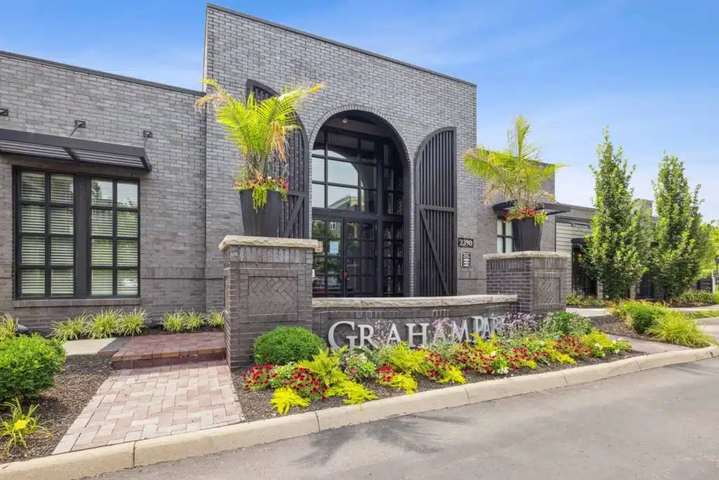 Modern brick building with large arched entrance, landscaped flower beds, and a sign that reads "Graham Park" at the front.