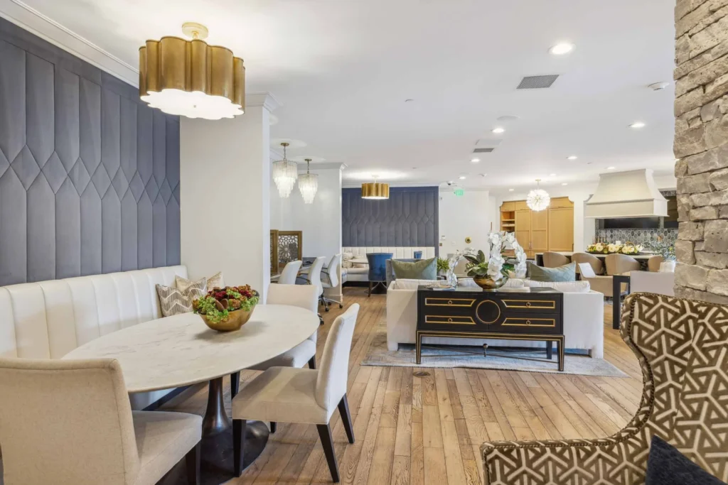 Modern, open-concept living and dining area with wooden floors, upholstered chairs, a round dining table, neutral tones, and contemporary light fixtures.